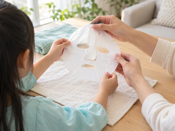 아쿠아색 옷을 입은 아이와 보호자가 무지 흰색 시트 마스크를 펼치는 손